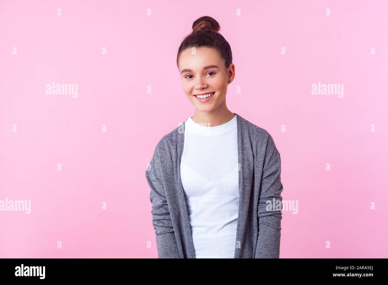Portrait of beautiful brunette teenage girl with bun hairstyle in casual pullover and T-shirt looking with joyous happy expression, clean fresh face s Stock Photo