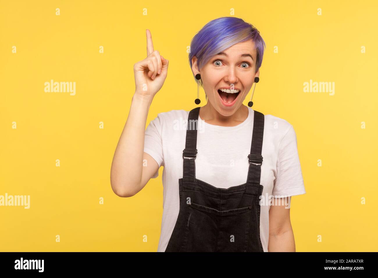 Eureka! Portrait of enthusiastic hipster girl with violet short hair in denim overalls pointing finger up, having great idea solution, creative smart Stock Photo
