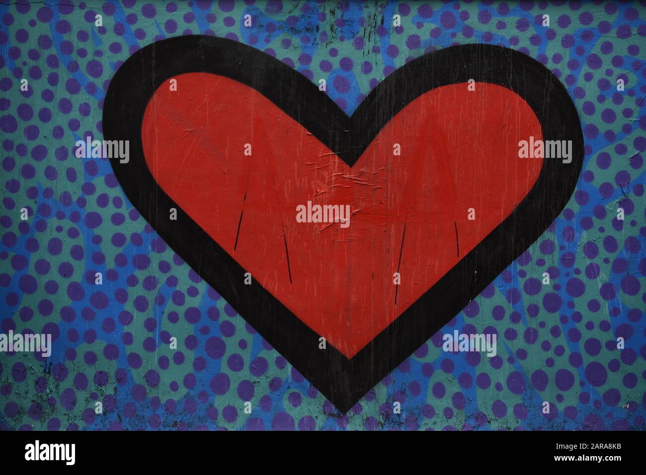Red heart with a black background painted on a wall. Background is purple dots, paint slighty peeling. Grunge feel. Abstract and concept useage. Stock Photo