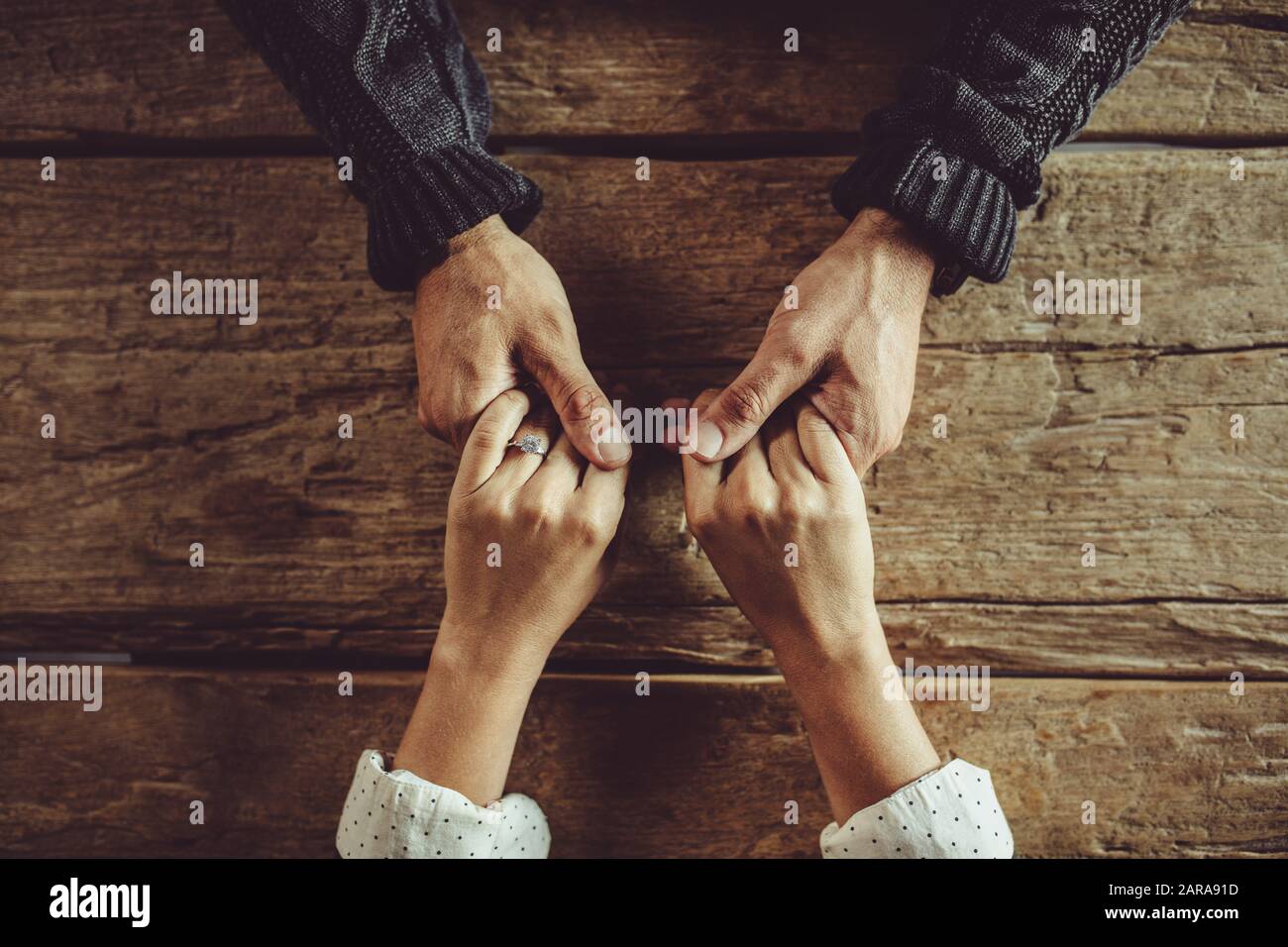 Directly above shot of couple sitting around table holding hands. Close-up shot of man and woman in love holding hands over a wooden table. Stock Photo