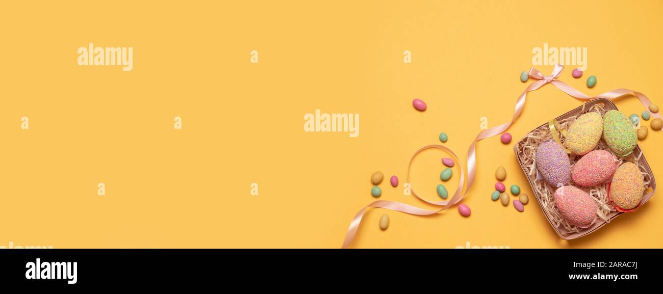 Happy easter composition. Decor eggs in a wooden wicker basket and sweet candy on a yellow background. Can be used for web banner, poster, voucher. Stock Photo