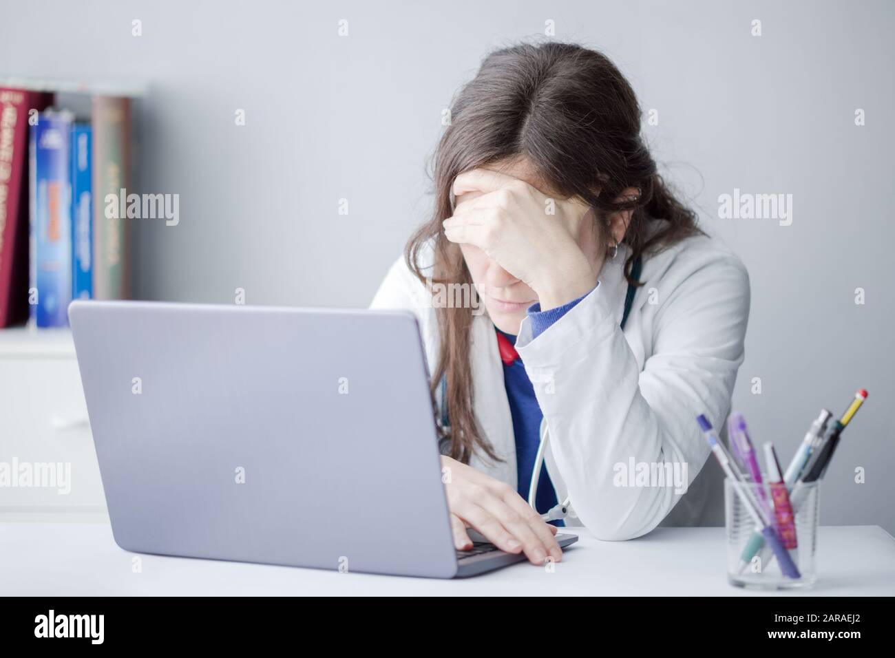 Tired Young Woman Doctor Working with a Laptop in a Clinic Stock Photo