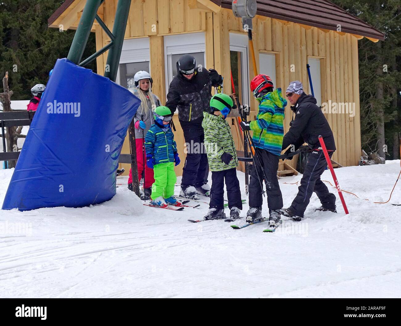 Children skiers get help by attendant on T-bar surface ski lift. Rogla ski resort, Slovenia. Stock Photo