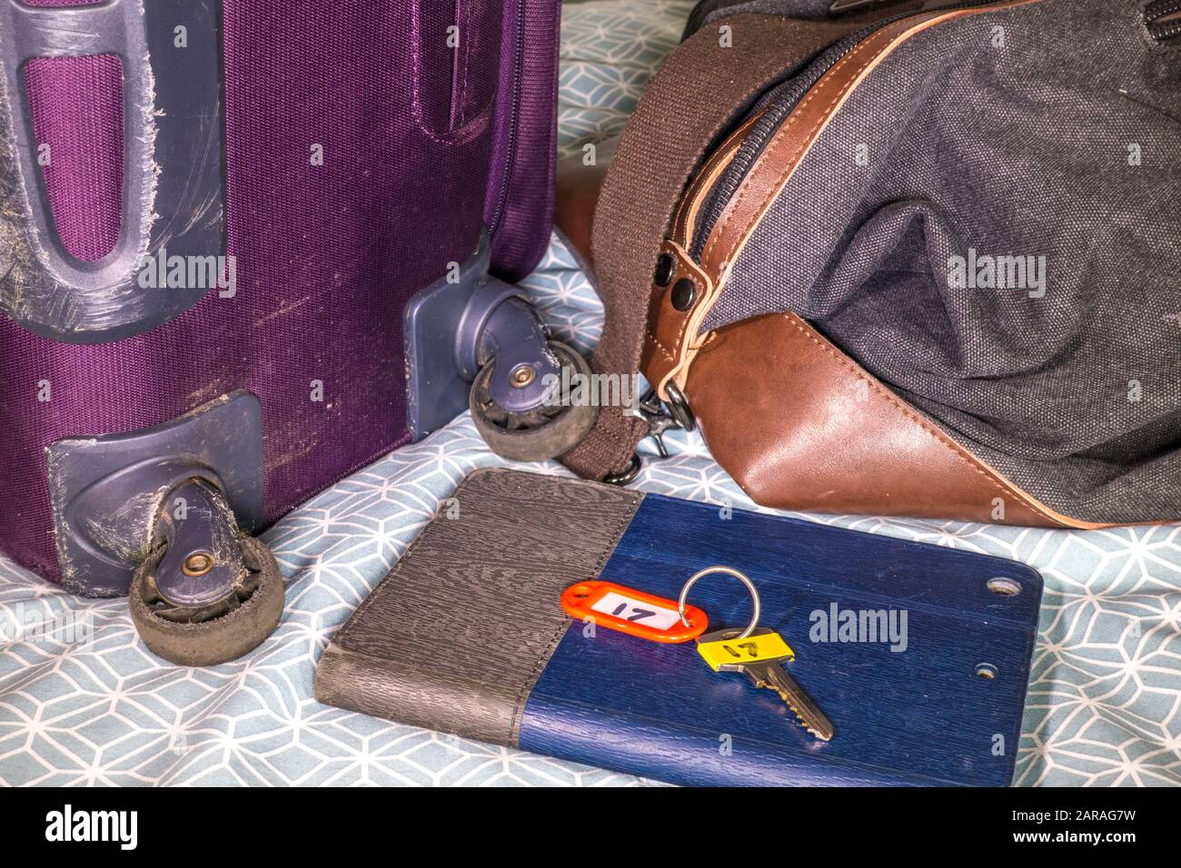 Suitcase, holdall, tablet computer and room key on a bed in a hotel room / motel, having just