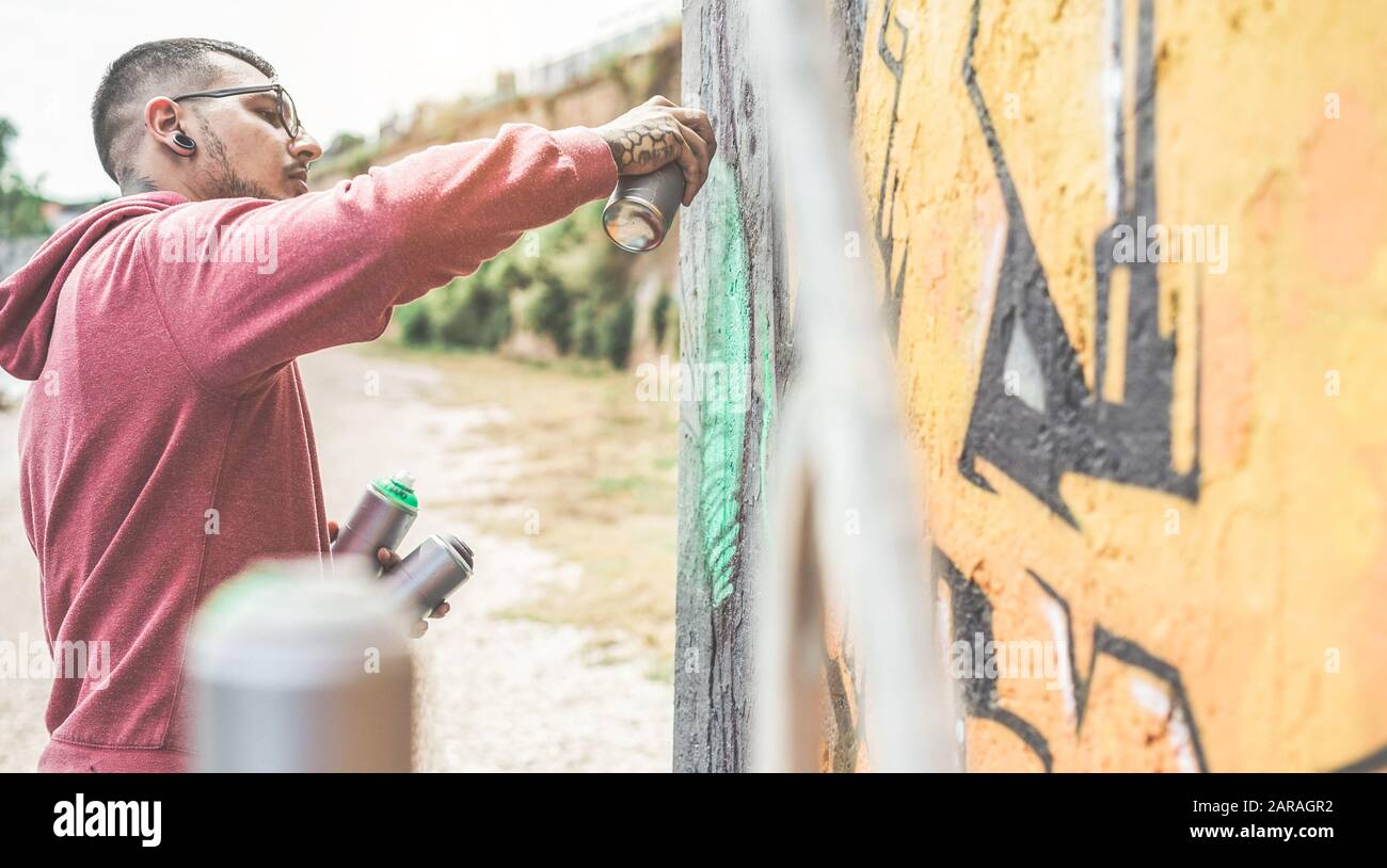 Young street artist painting with color spray on the wall ...