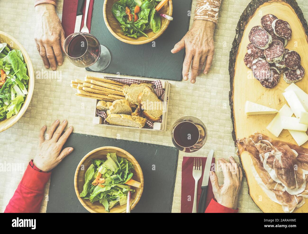 Top view of senior friends eating salad ,salami,cheese and italian ham - Old people toasting red wine for dinner at restaurant - Focus on up woman rig Stock Photo