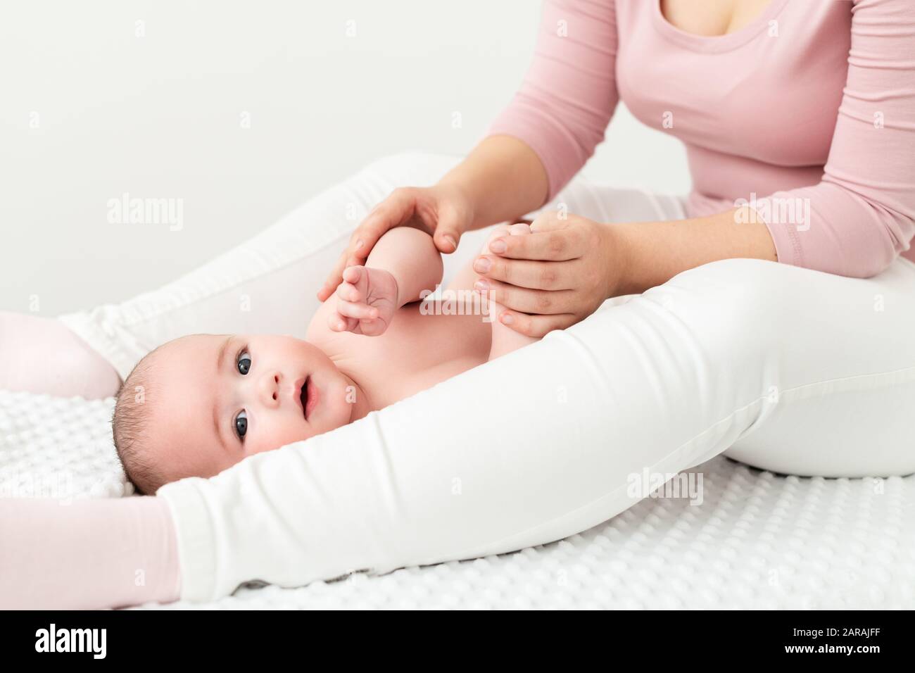 Baby massage background. Mother gently massaging her baby boy. Baby lying on back and looking at camera during massage. Stock Photo