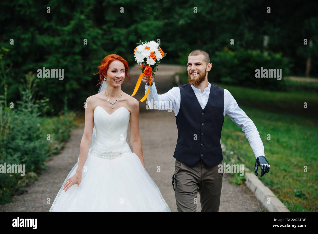 Exited newly wed couple walking down the path through a park Stock Photo