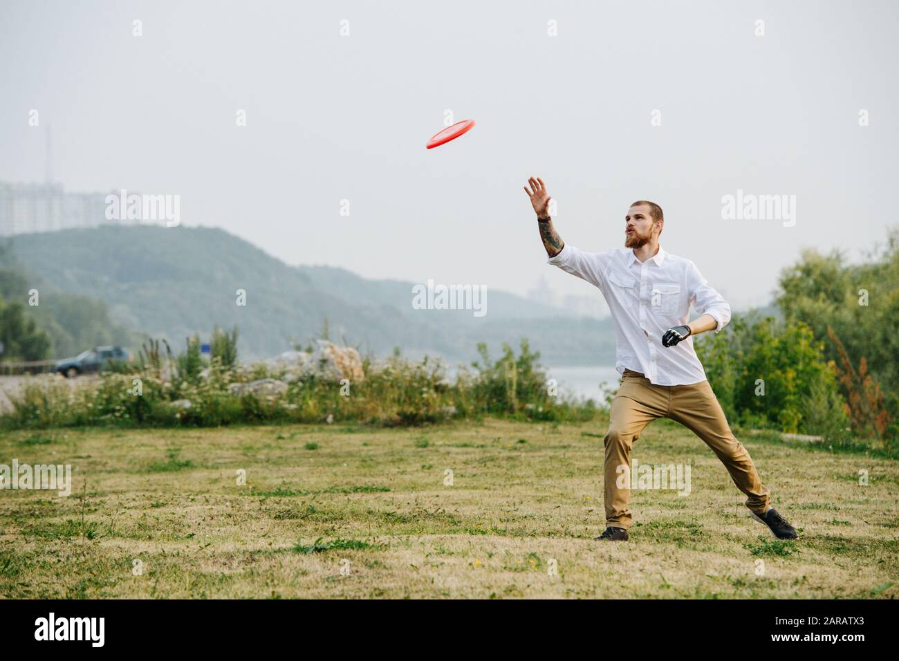Man catching frisbee in a park next to a river and forest ridge Stock Photo