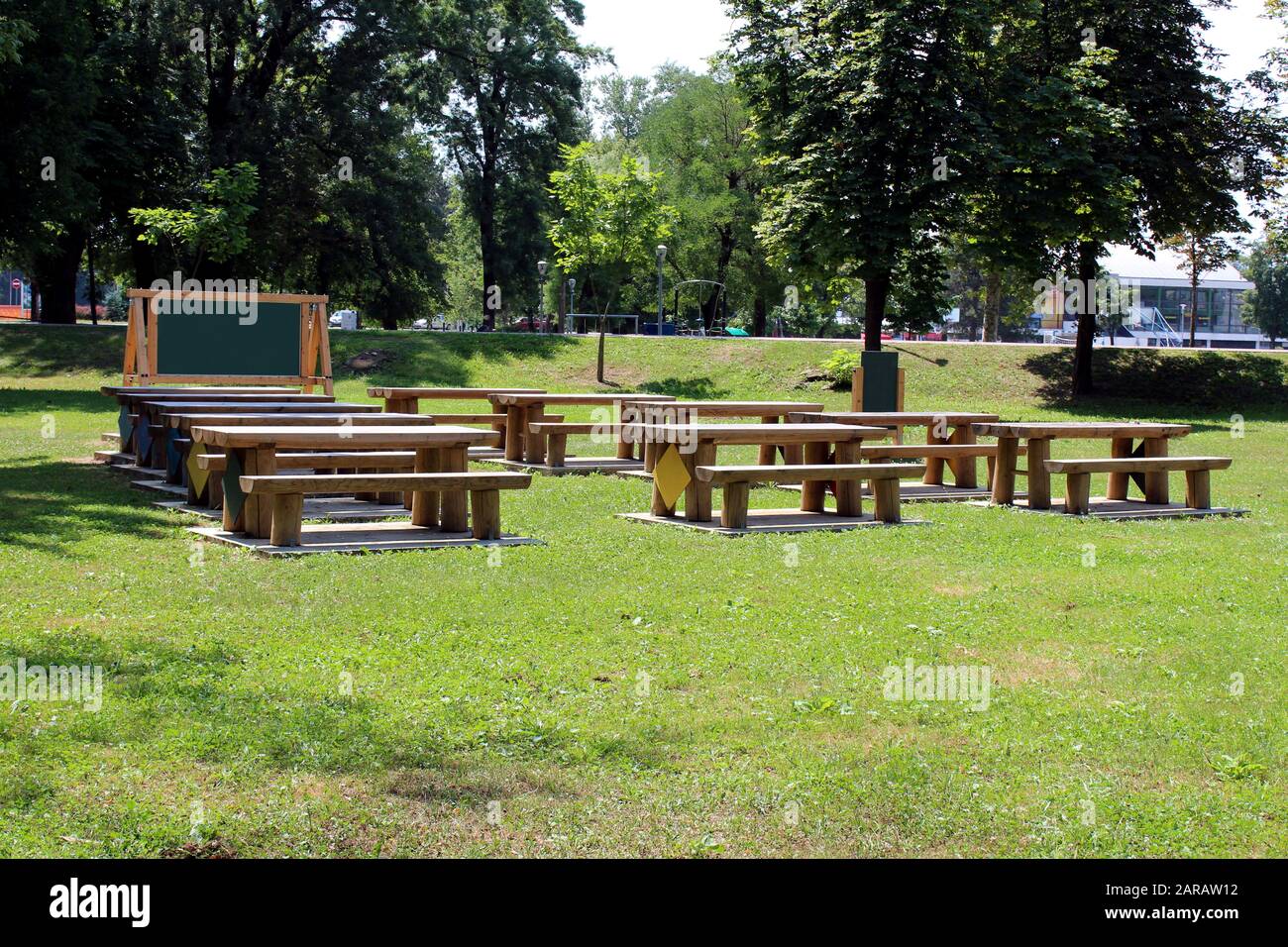 Outdoor classroom with blackboard tables and benches made from strong wooden logs in local public park surrounded with grass and tall trees Stock Photo
