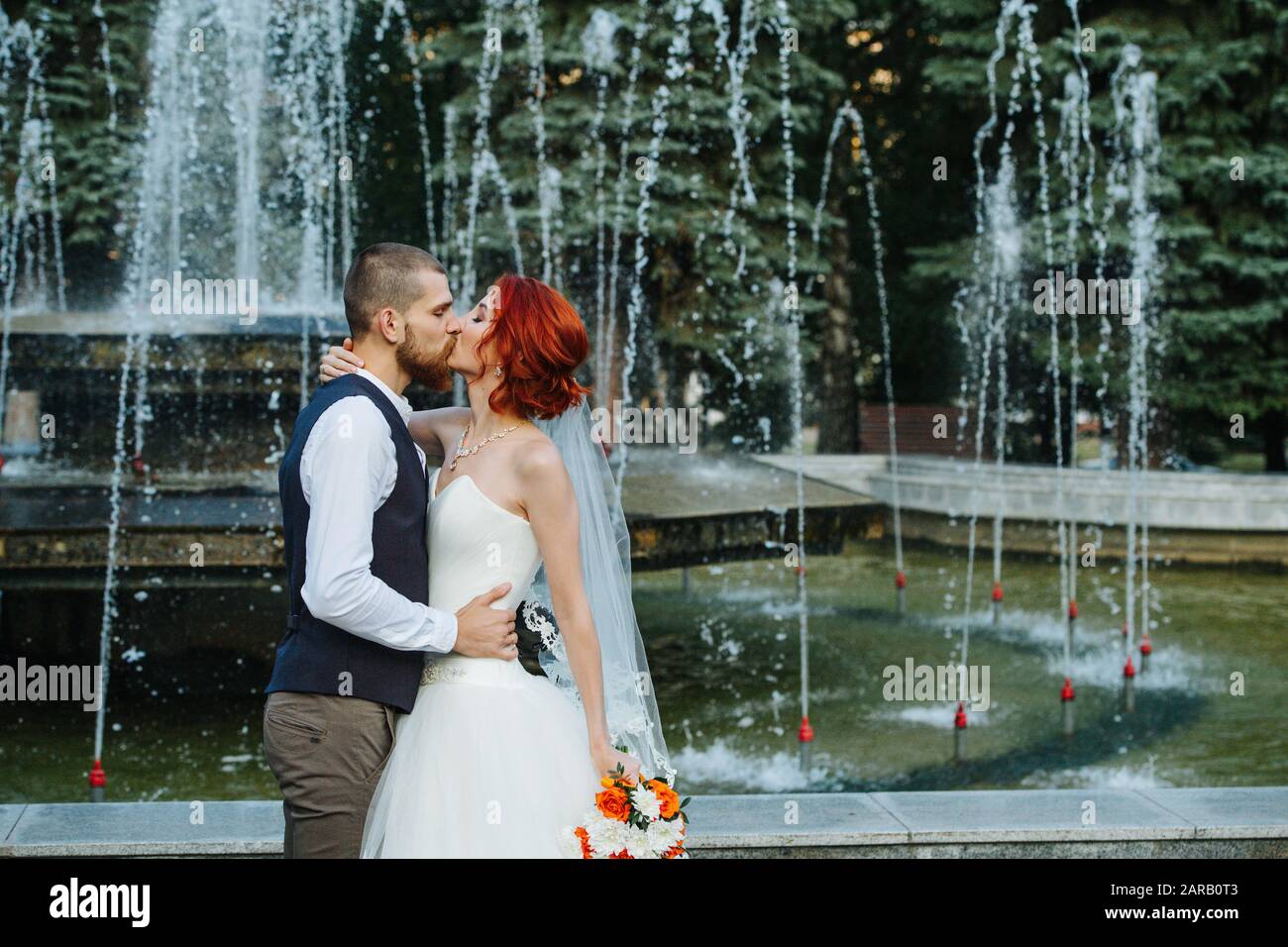 The bride and groom kissing in front of a fountain. Stock Photo