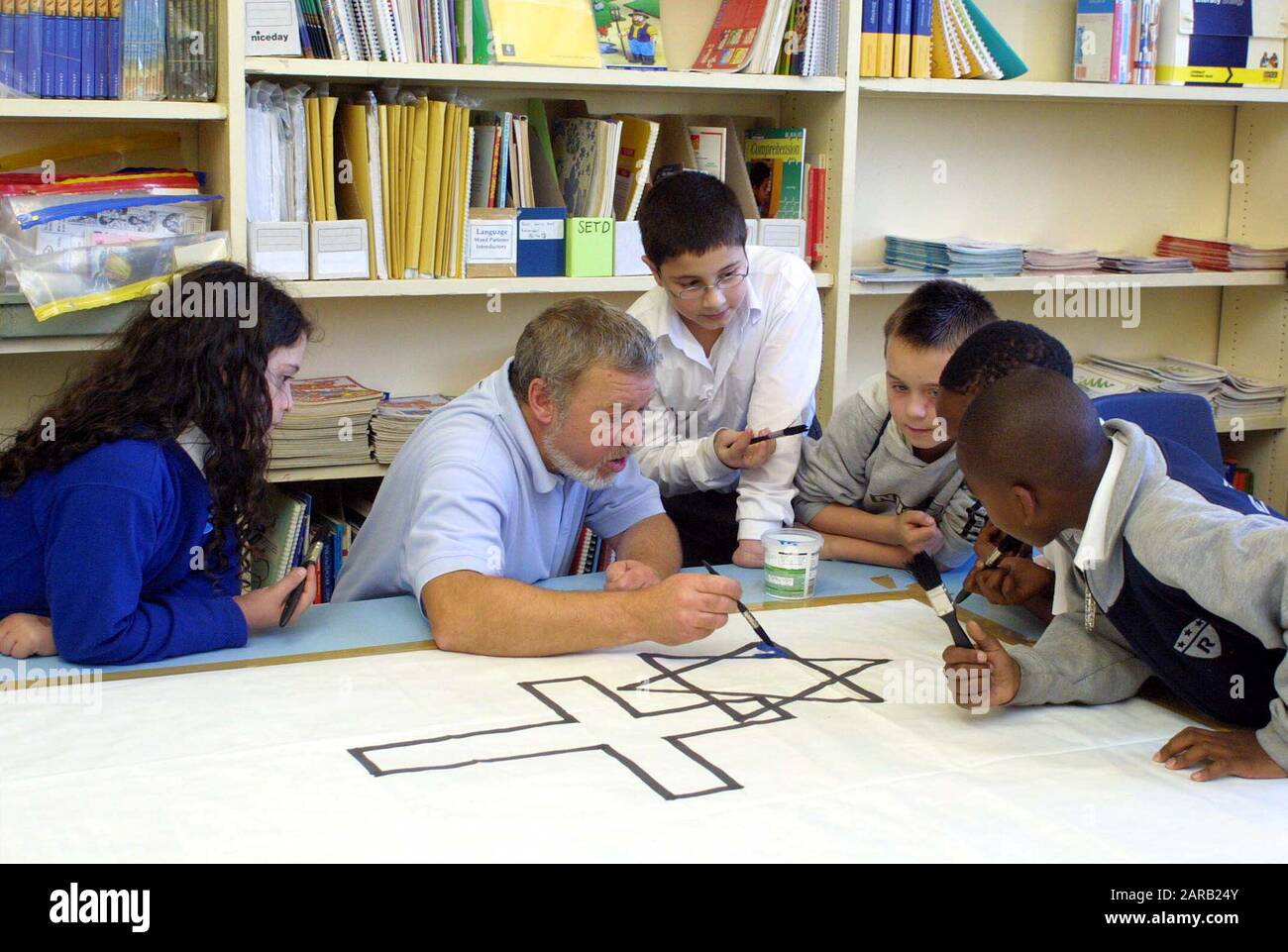 Male teacher working with multi ethnic group of primary uniformed students on a Religion lesson Stock Photo