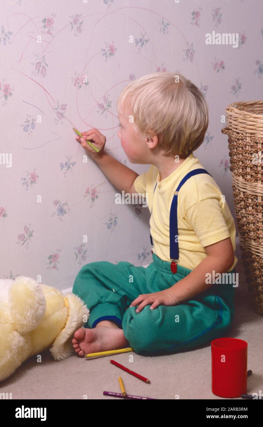 small boy drawing on his bedroom wall with pencil crayons Stock Photo