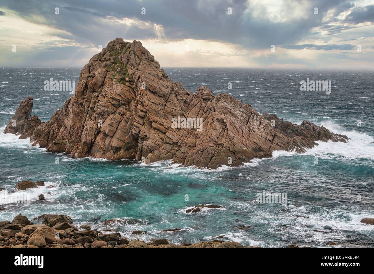 Sugar Loaf Rock in the Indian Ocean is framed by rough seas and heavy storm clouds on the wild Western Australian coastline. Stock Photo