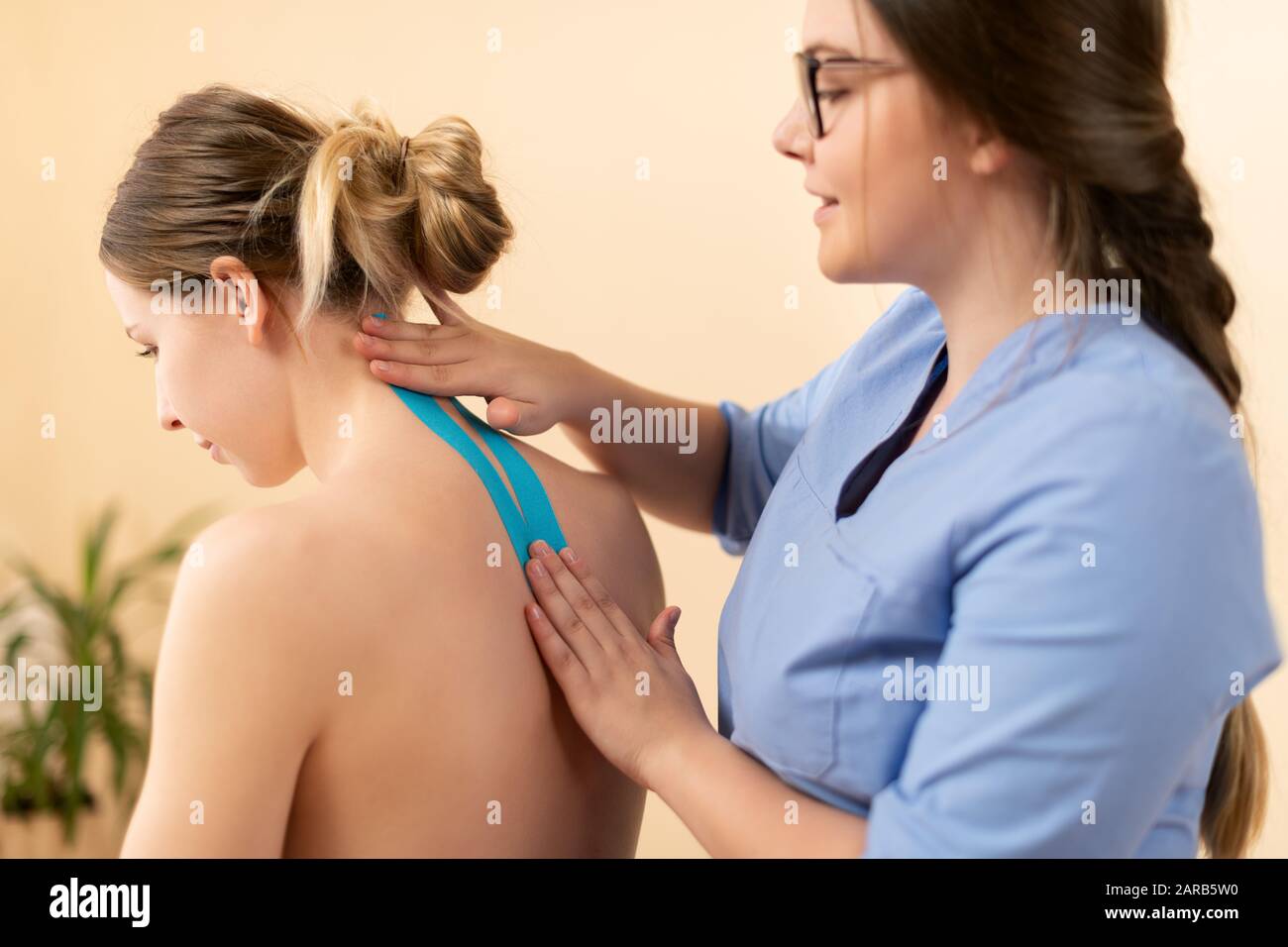 Female physiotherapist applying kinesio tape on patient's neck. Kinesiology, physical therapy, rehabilitation concept. Side view. Stock Photo