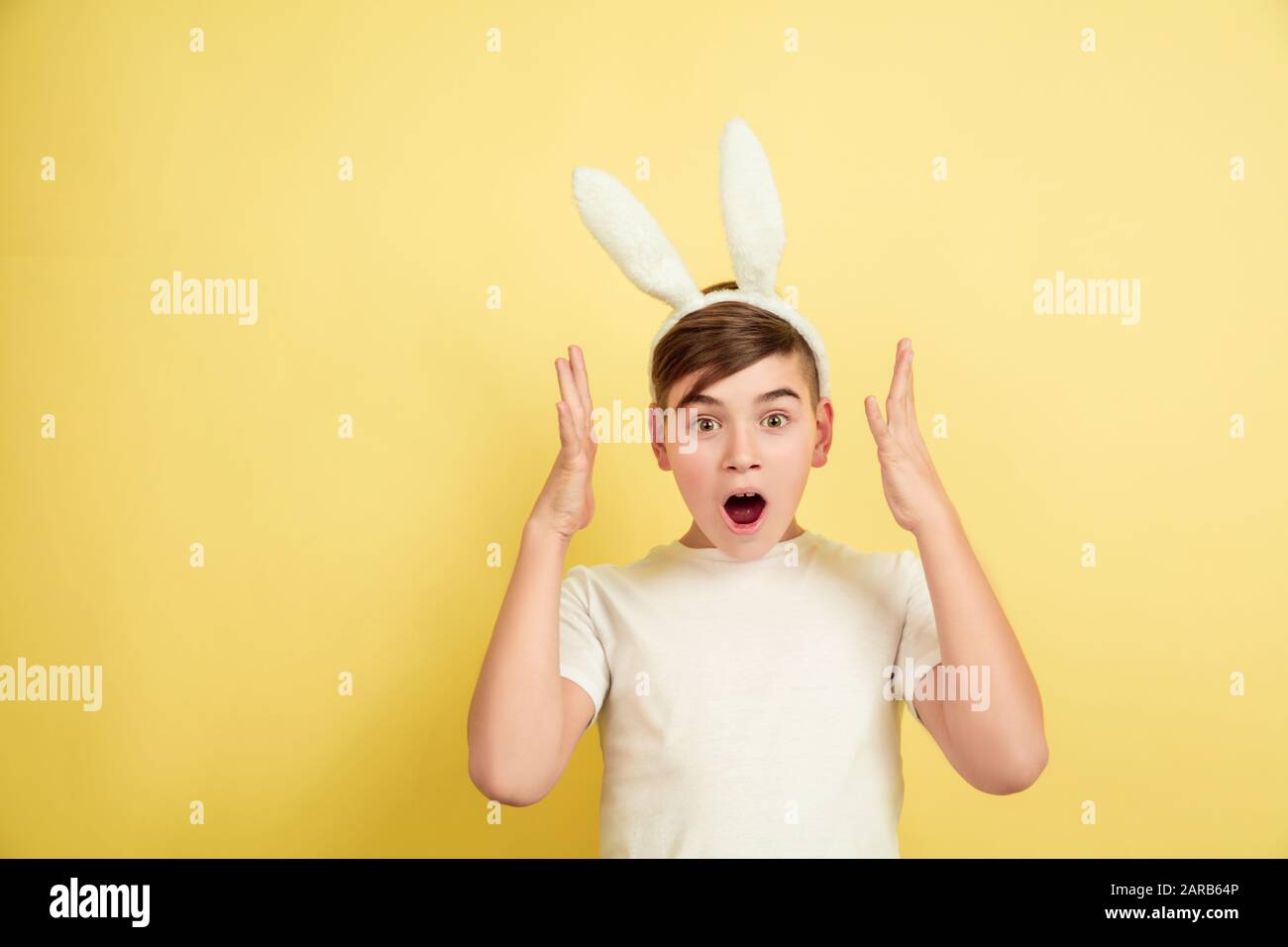 Shocked, astonished, wondered. Caucasian boy as an Easter bunny on yellow background. Happy easter greetings. Beautiful male model. Concept of human emotions, facial expression, holidays. Copyspace. Stock Photo