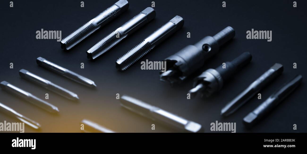 Closeup straight flute tap tip and hole saw on dark background.  Industrial tapping tools. Carbide tip metal cutter. Metalworking hardware. Mechanic Stock Photo