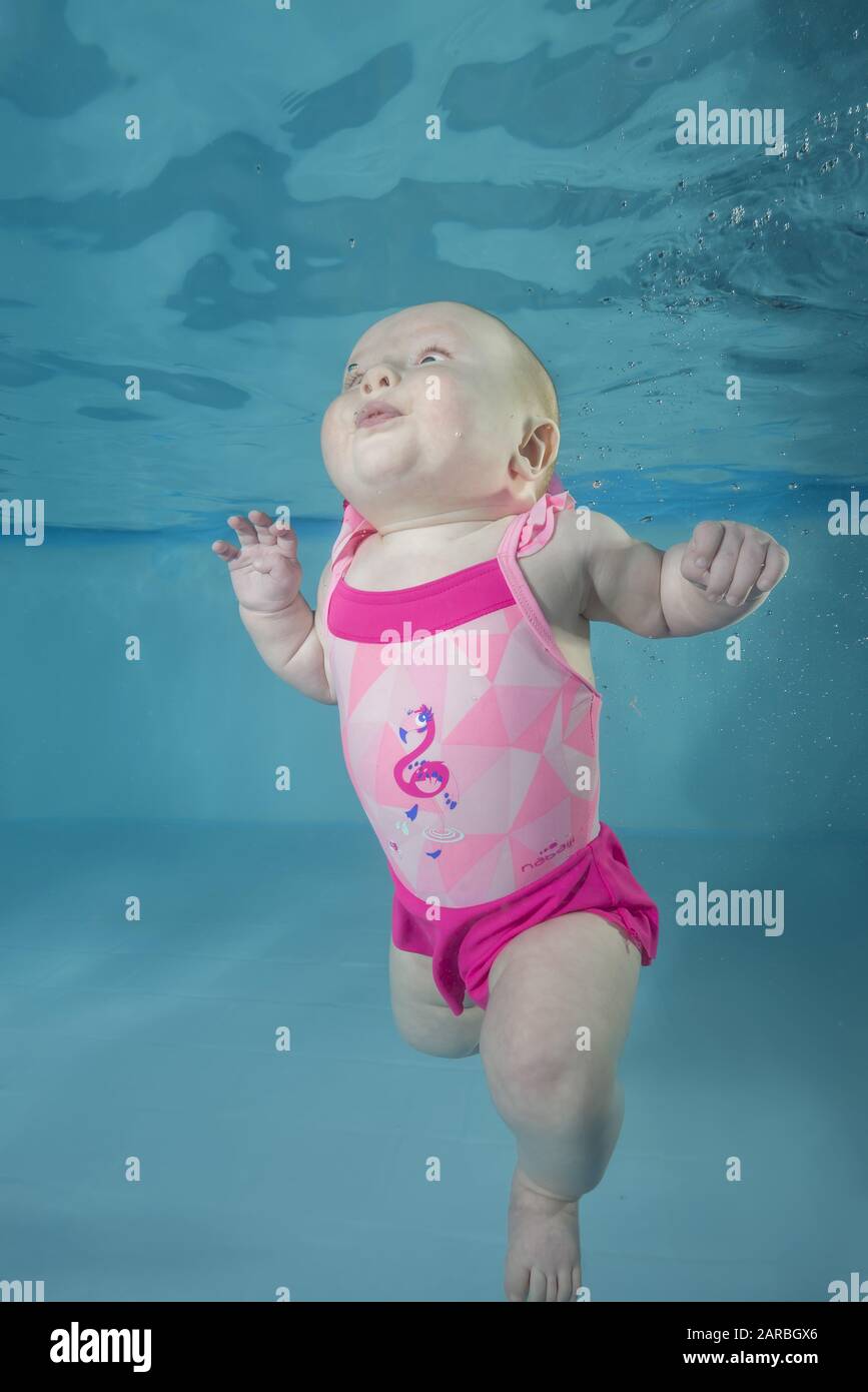 Little baby girl in pink swimsuit learns to swims underwater. Baby