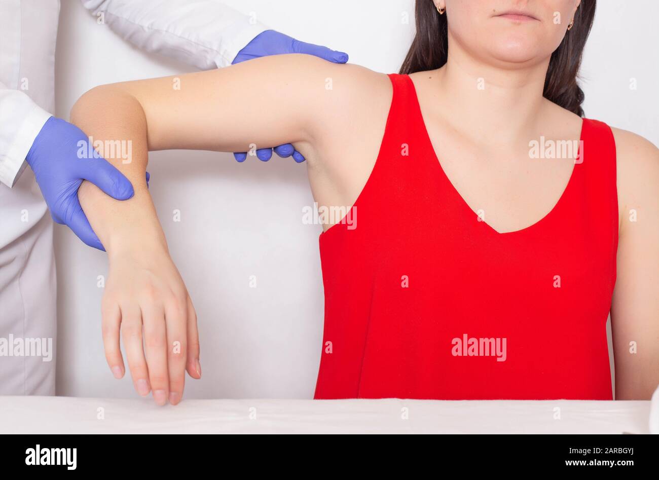 Doctor traumatologist examines a broken shoulder in a girl athlete. The concept of injury in athletes, dislocation of the shoulder, luxation Stock Photo