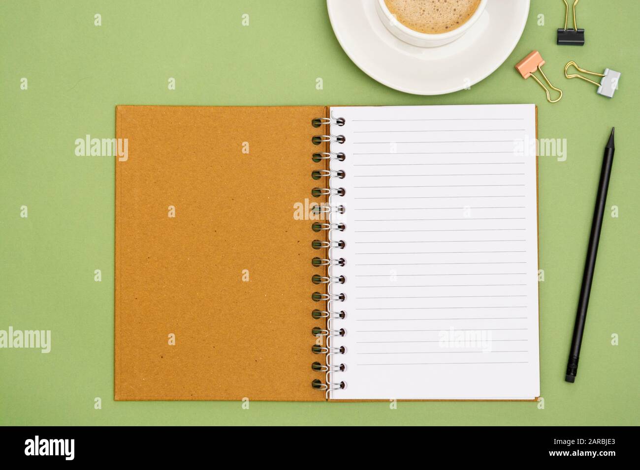 Open notebook with empty page and coffee cup. Table top, work space on green background. Creative flat lay. Stock Photo