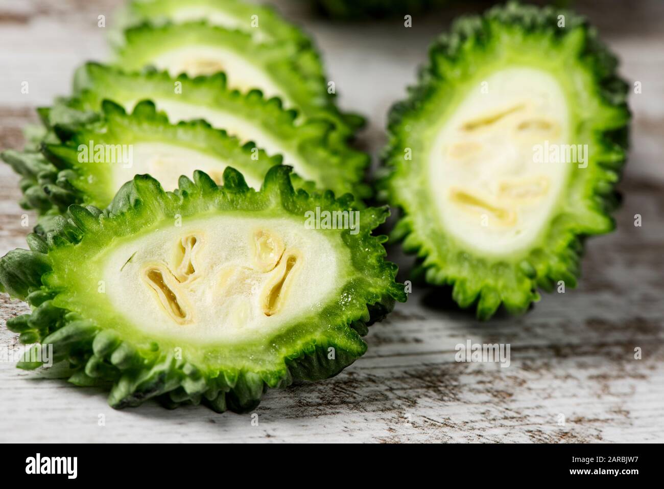 closeup of some slices of raw karela, also known as bitter melon or bitter gourd, on a white rustic wooden table Stock Photo