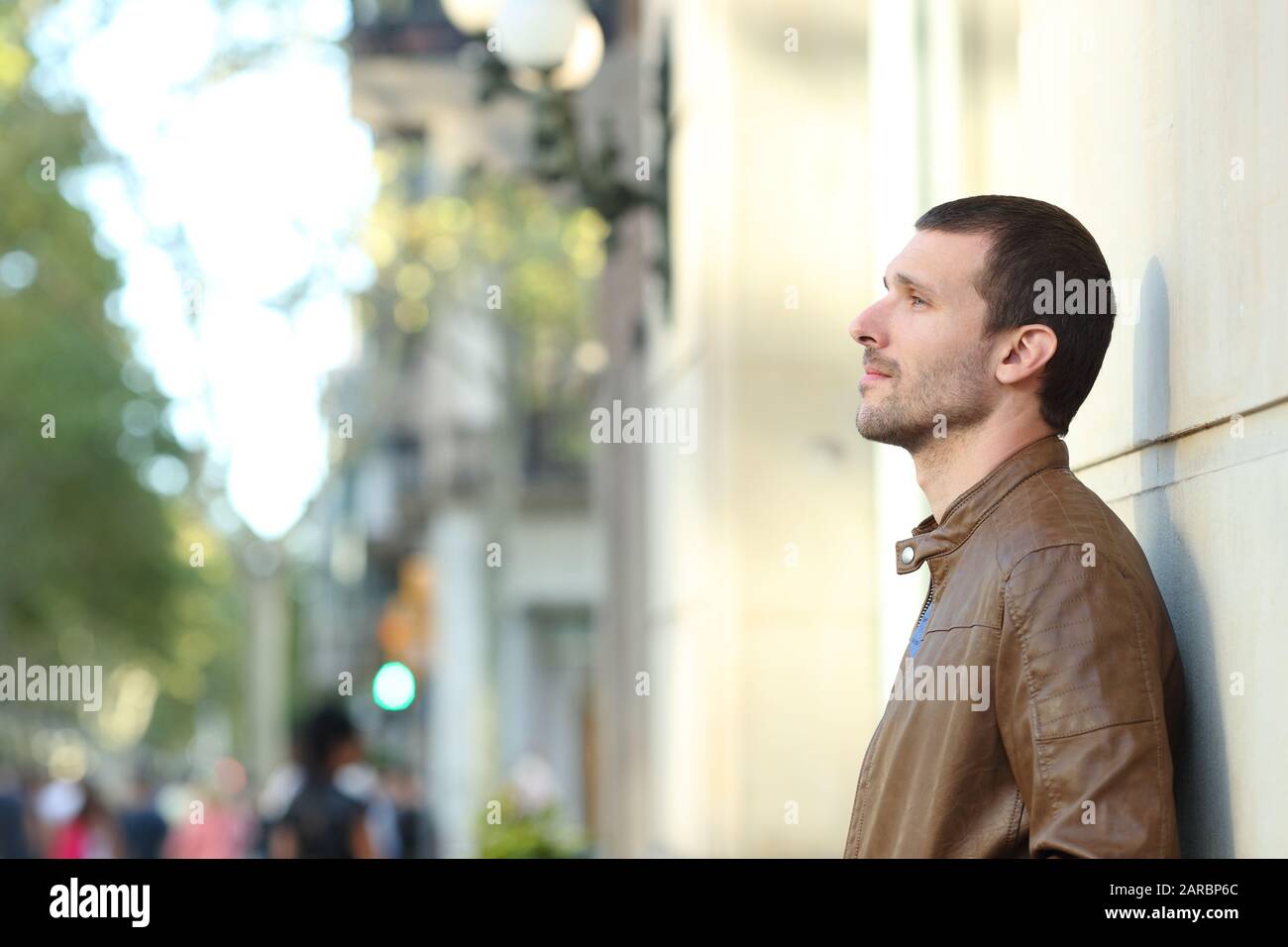 Profile of a pensive adult man looking away leaning in a wall in the street Stock Photo