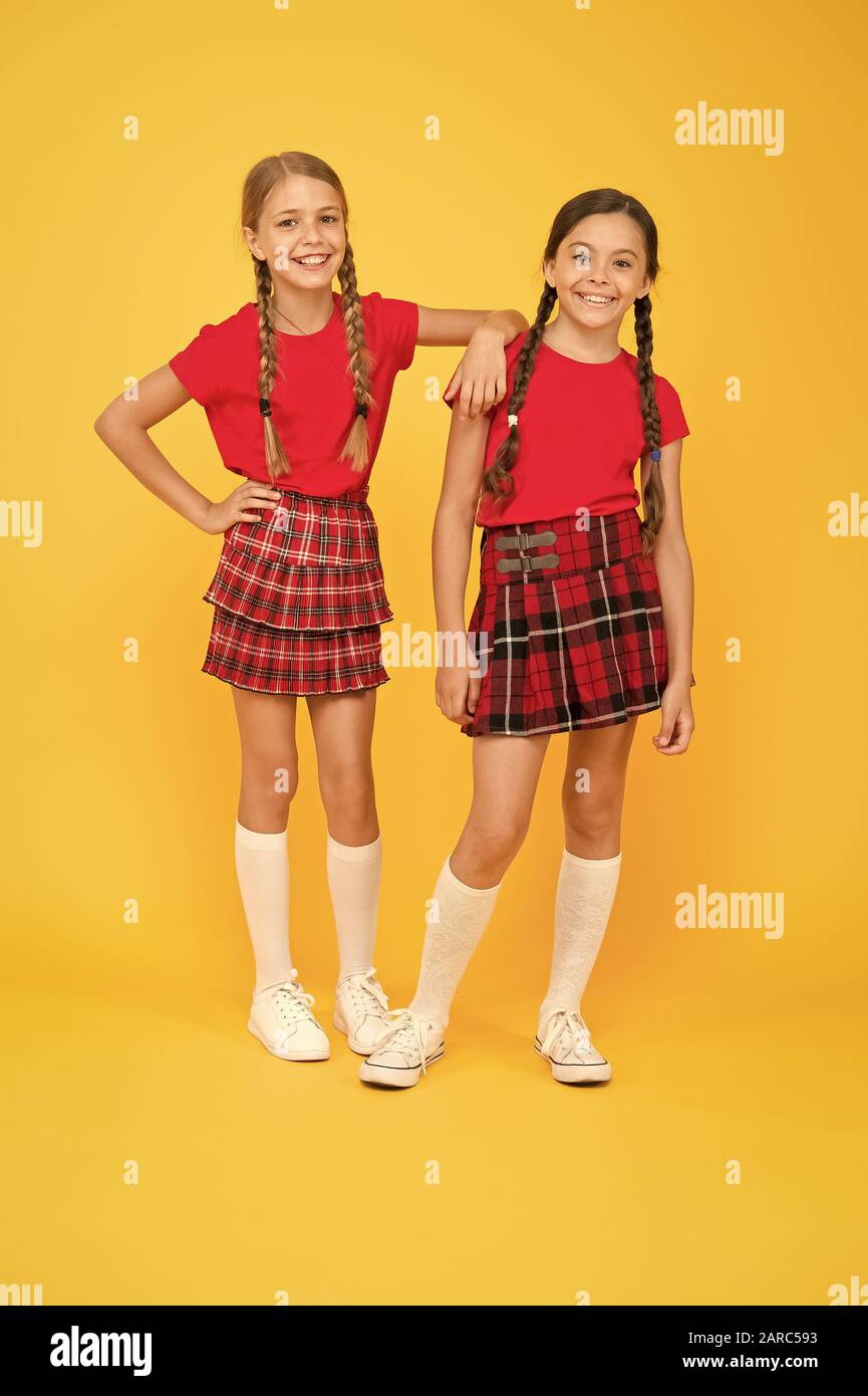 Enjoying playtime. childhood happiness. trendy school uniform. red fashion  girls. english style fashion. happy little girls in checkered skirt. beauty  look. happy children on yellow background Stock Photo - Alamy