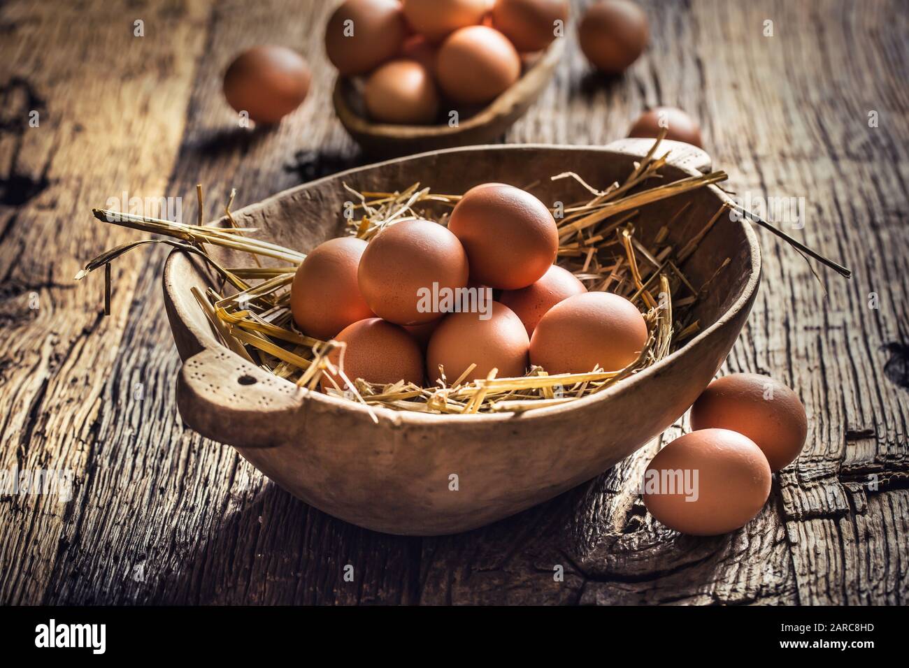 Fresh raw eggs in straw and wooden bowl on rustic wooden table Stock Photo