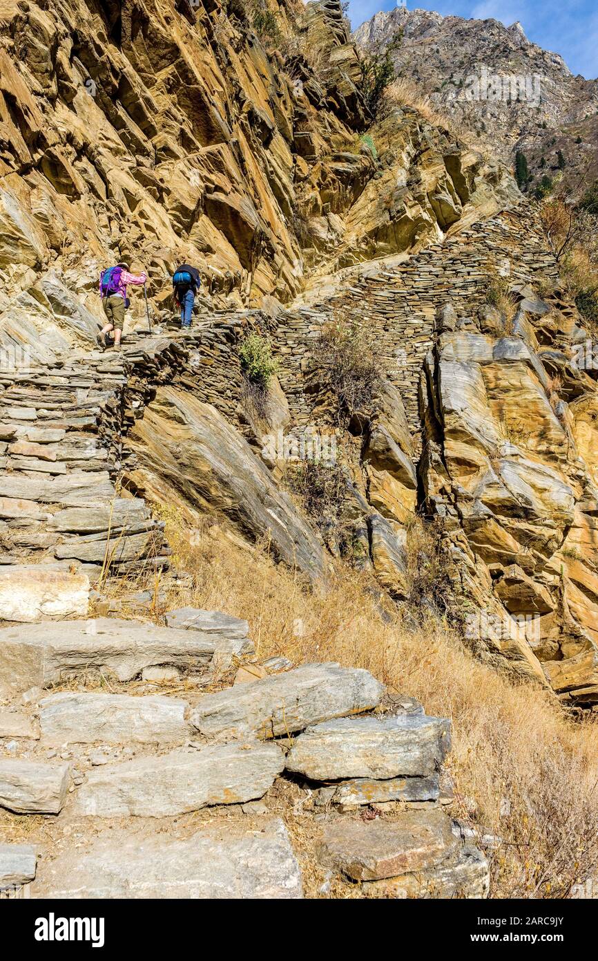 Trekkers on a stone-built trail across a mountainside in the Dolpo Himalayas, Nepal Stock Photo