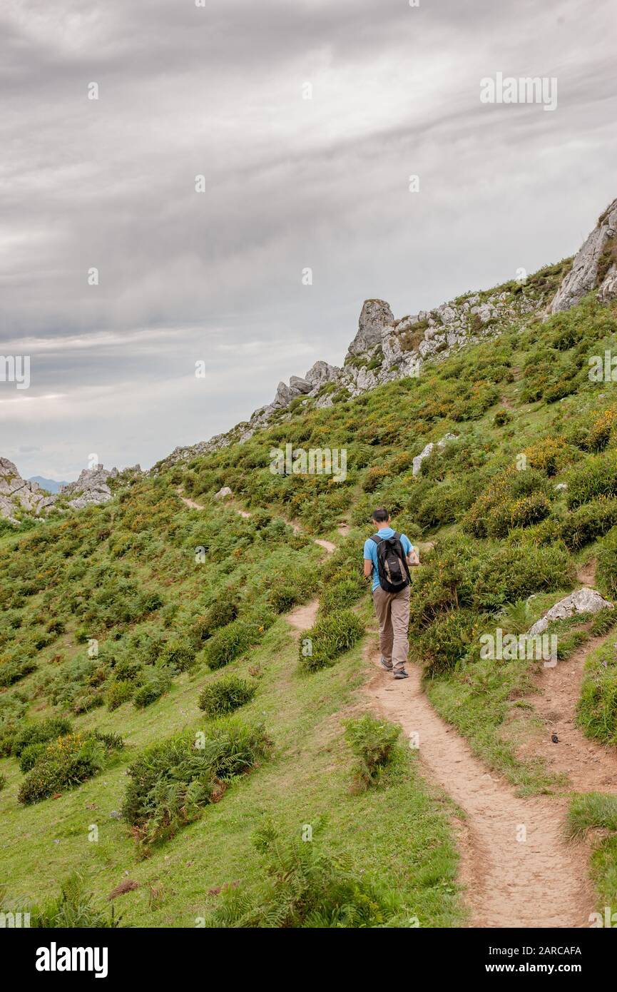 A man with a rocksack hiking along a narrow footpath in stoney ...