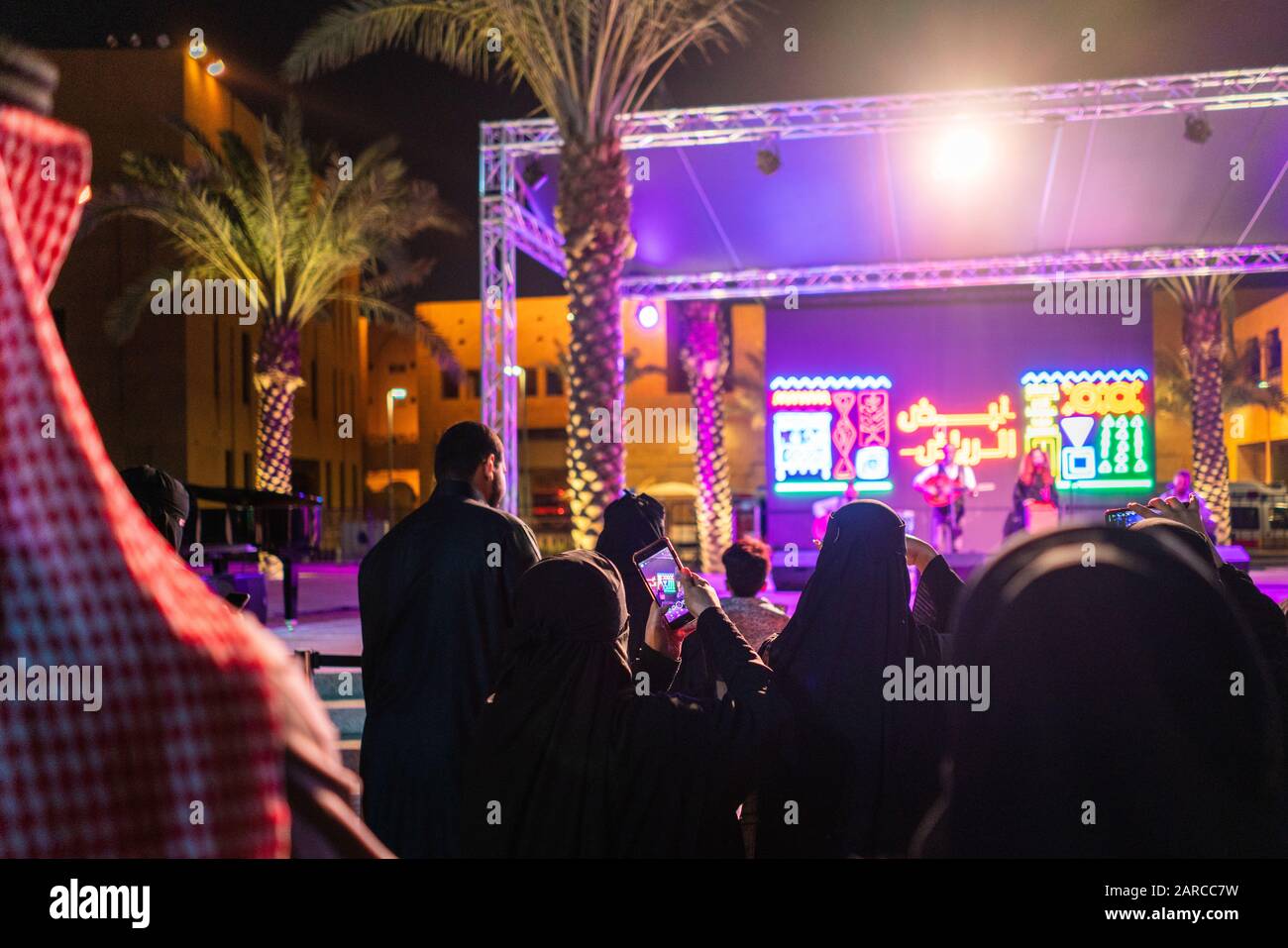 Families in Riyadh, Saudi Arabia enjoying a legal public concert and recording video on mobile phones at night Stock Photo