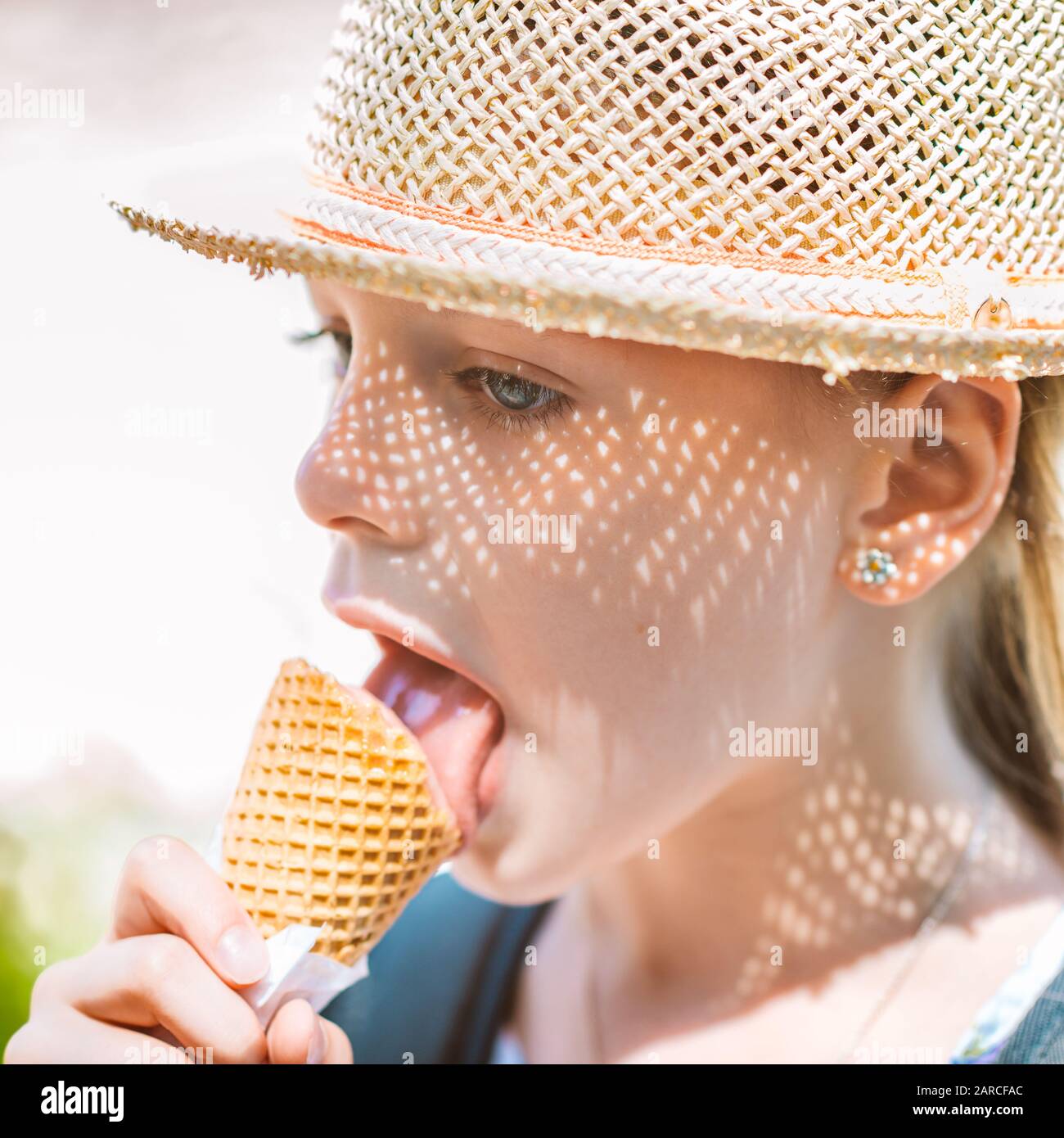 Little girl in a straw hat eating ice cream in a cone on a summer sunny ...