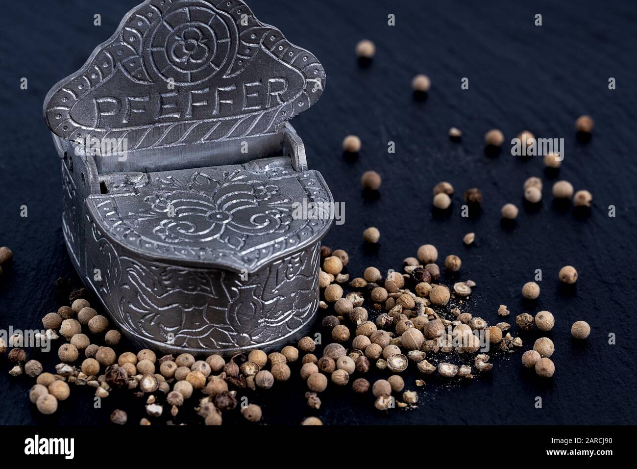 Whole and crushed peppercorns lying around a pewter storage jar on a slate plate Stock Photo