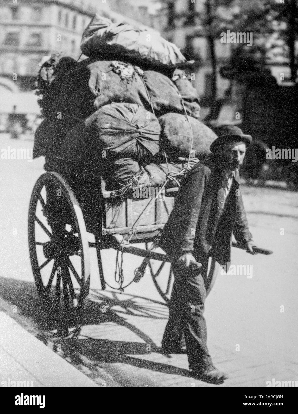 19th century photo of rag-and-bone man / ragpicker pulling hand cart / handcart loaded with unwanted rags, metal and other household waste in city Stock Photo