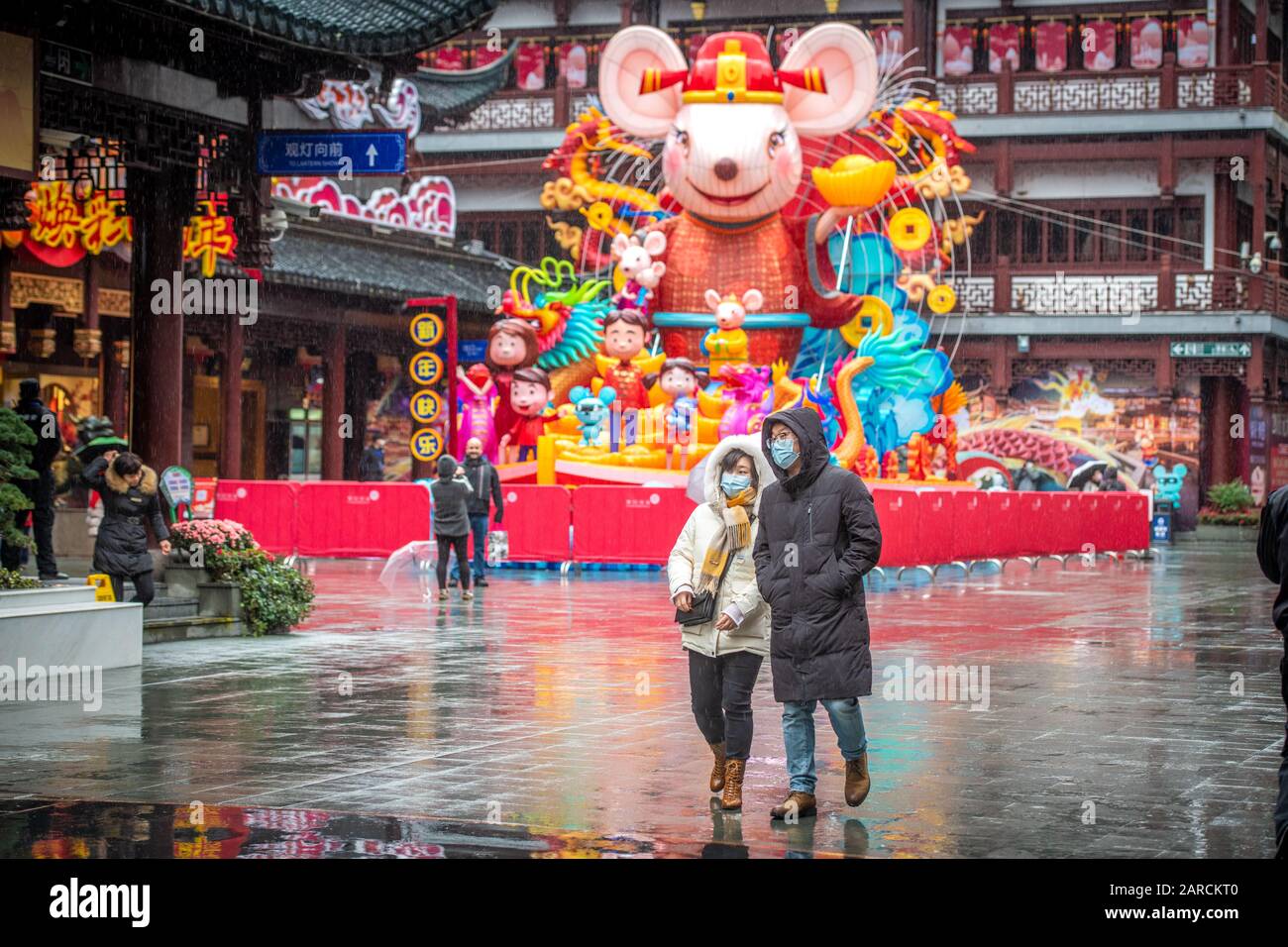 Shanghai, China, 25th Jan 2020, A woman and man in masks walks with Chinese New Year celebration reminders around them Stock Photo