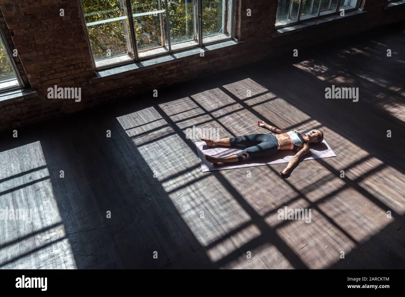 Young calm woman practicing yoga lying in dead body pose relax on mat in studio Stock Photo