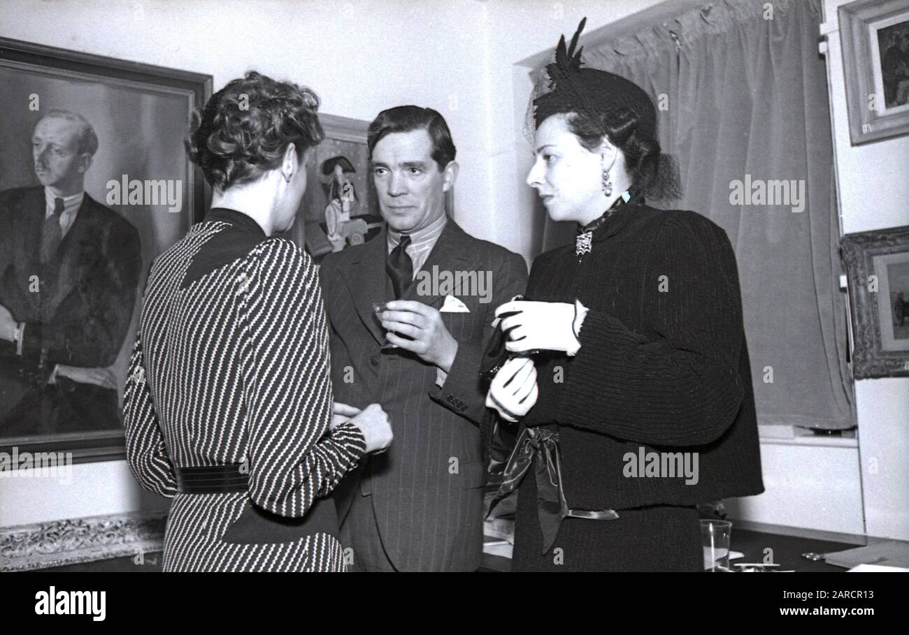 1940s, historical, guests in conversation at a drinks party at a London art Gallery, London, England, UK, showing the fashions of the day, with one lady wearing a stylish hat. Stock Photo