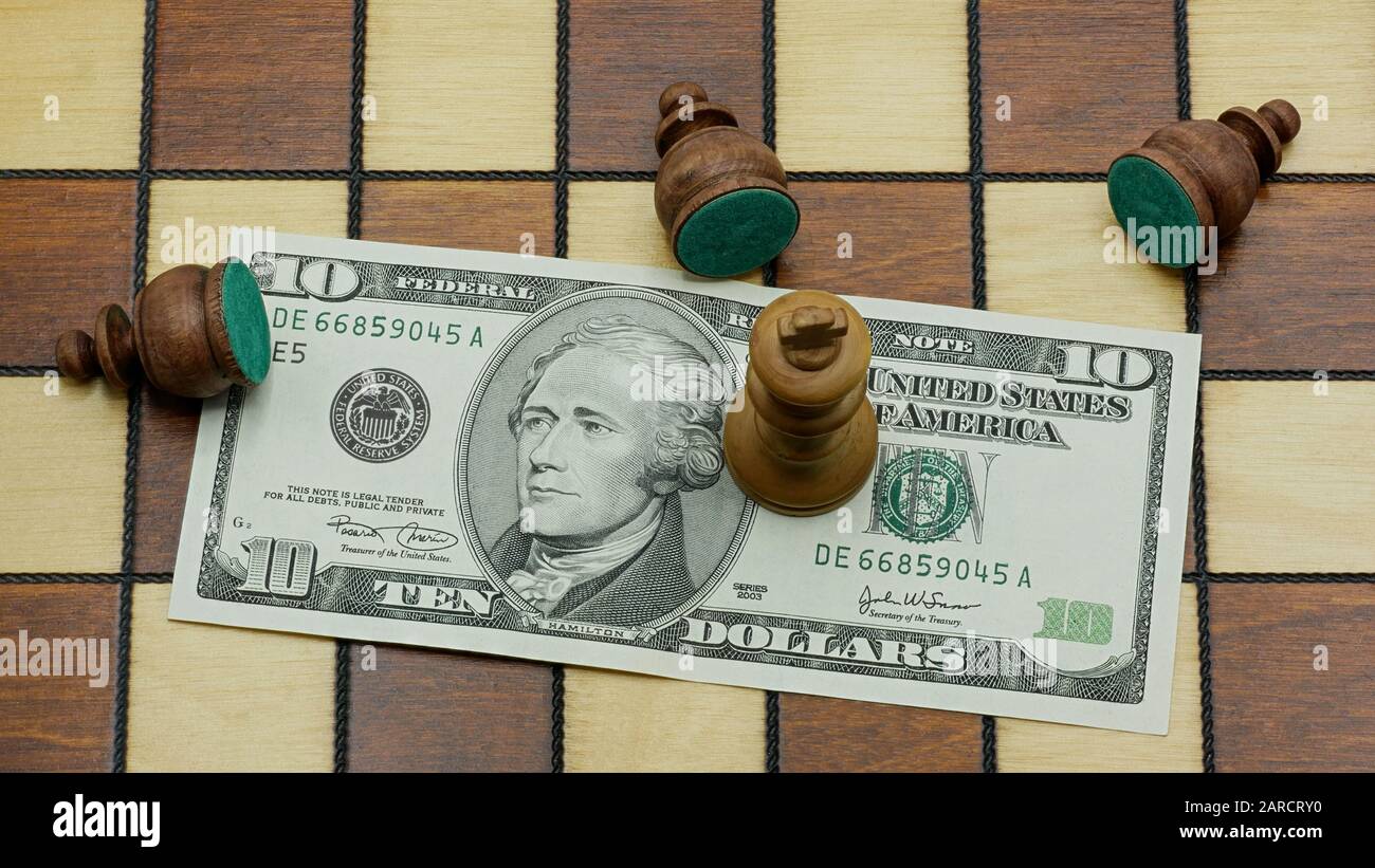 Money Rules: Defeated Black Pawn Chess Pieces Lying Around A White King Standing On A 10 Dollars Banknote On A Chess Board Stock Photo