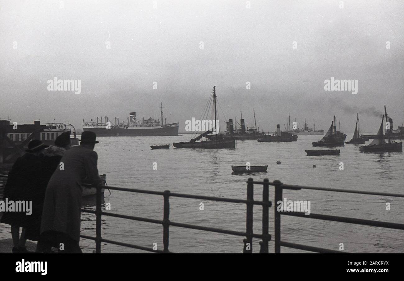 1940s, historical, father, mother and daughter in Gravesend, Kent, England, UK, looking at the harbour and the moored boats including a steamship. Until the building of the Tilbury docks in 1886, Gravesend was the Thames's first port of entry. Stock Photo