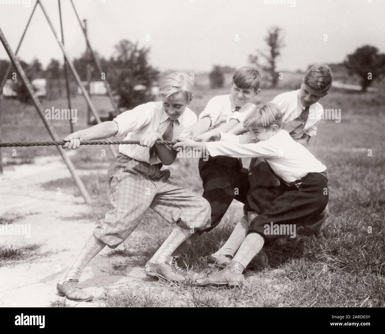 1930s 4 BOYS  PULLING ON ROPE PLAYING TUG OF WAR ON PLAYGROUND ALL WEARING SHORT PANTS KNICKERS SOCKS WHITE SHIRTS TIES - b12009 HAR001 HARS KNICKERS JOY LIFESTYLE SATISFACTION RURAL HEALTHINESS ATHLETICS COPY SPACE FRIENDSHIP FULL-LENGTH PHYSICAL FITNESS MALES ATHLETIC CONFIDENCE B&W ACTIVITY PHYSICAL HIGH ANGLE STRENGTH EXCITEMENT RECESS RECREATION SHIRTS PRIDE ON CONNECTION CONCEPTUAL ATHLETES FLEXIBILITY MUSCLES STYLISH TIES TUG-OF-WAR COOPERATION GROWTH JUVENILES PRE-TEEN PRE-TEEN BOY TOGETHERNESS BLACK AND WHITE CAUCASIAN ETHNICITY HAR001 OLD FASHIONED TUG Stock Photo
