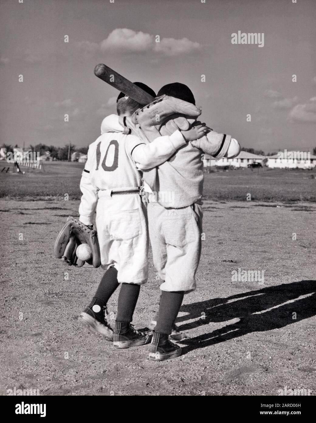 1960s BACK VIEW TWO BOYS ARM IN ARM BACK VIEW WEARING LITTLE LEAGUE BASEBALL UNIFORMS - b14309 HAR001 HARS JOY LIFESTYLE BROTHERS HEALTHINESS ATHLETICS COPY SPACE FRIENDSHIP FULL-LENGTH INSPIRATION CARING MALES ATHLETIC SNEAKERS B&W ACTIVITY HAPPINESS PHYSICAL STRENGTH PALS ARM IN ARM RECREATION REAR VIEW UNIFORMS CONNECTION CONCEPTUAL ATHLETES FLEXIBILITY FRIENDLY MUSCLES SUPPORT BEST FRIEND BACK VIEW BALL GAME BALL SPORT COOPERATION GROWTH JUVENILES RELAXATION TOGETHERNESS WALKING AWAY BASEBALL BAT BEST FRIENDS BFF BLACK AND WHITE CAUCASIAN ETHNICITY HAR001 OLD FASHIONED Stock Photo