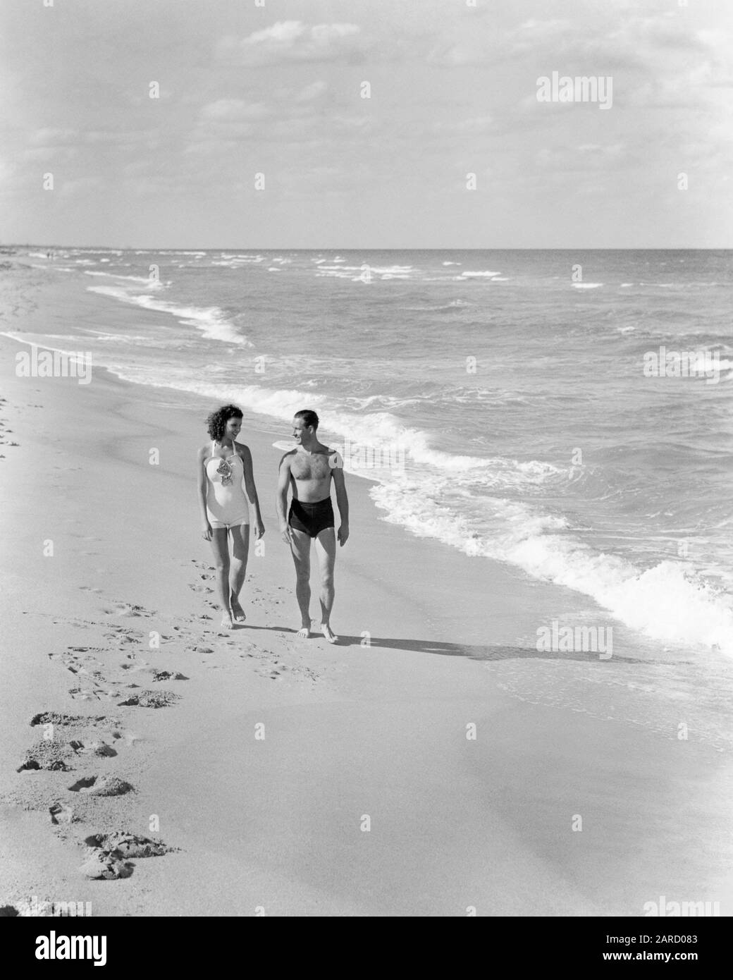 1930s 1940s COUPLE WEARING BATHING SUITS WALKING TALKING TOGETHER ON BRIGHT WARM SUNLIT SEASHORE OCEAN BEACH SAND - b7062 HAR001 HARS HEALTHY BALANCE STRONG JOY LIFESTYLE OCEAN SATISFACTION FEMALES MARRIED SPOUSE HUSBANDS HEALTHINESS COPY SPACE FRIENDSHIP FULL-LENGTH LADIES PERSONS SCENIC INSPIRATION CARING MALES SUNLIGHT WARM SERENITY B&W PARTNER FREEDOM ACTIVITY DREAMS HAPPINESS PHYSICAL BRIGHT WELLNESS HIGH ANGLE LEISURE STRENGTH RECREATION ON STROLLING CONCEPTUAL ESCAPE FLEXIBILITY MUSCLES SUNLIT BATHING SUITS PERSONAL ATTACHMENT AFFECTION EMOTION MID-ADULT MID-ADULT MAN MID-ADULT WOMAN Stock Photo