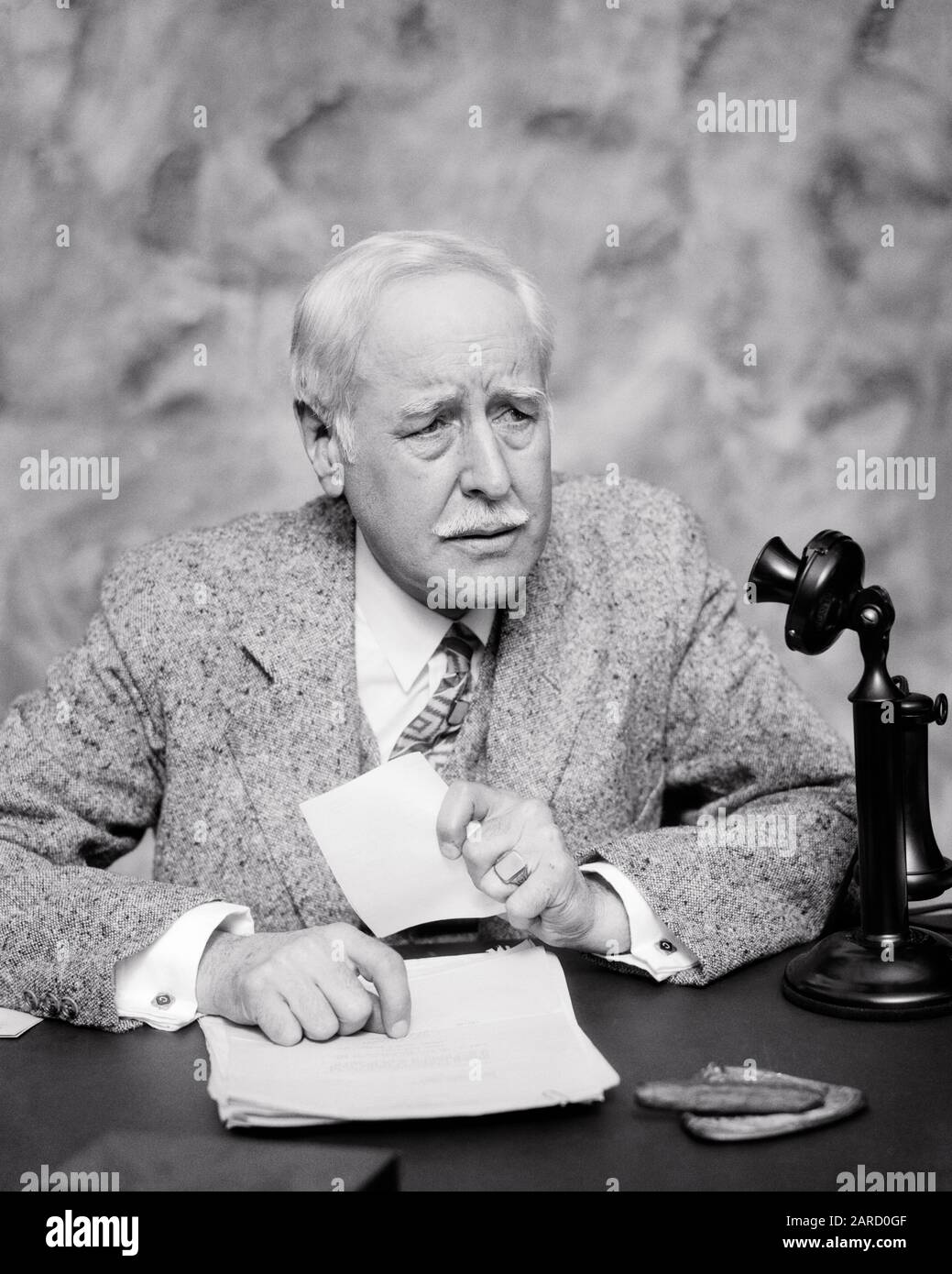 1920s MATURE BUSINESSMAN AT DESK CLUTCHING PAPER CONCERNED FACIAL EXPRESSION CIGAR IN ASHTRAY CANDLESTICK PHONE ON DESK - c3686 HAR001 HARS LIFESTYLE ELDER TWEED STUDIO SHOT MOODY COPY SPACE HALF-LENGTH PERSONS MALES RISK SENIOR MAN VEST SENIOR ADULT EXPRESSIONS TROUBLED B&W CONCERNED SADNESS CANDLESTICK MUSTACHE SUIT AND TIE OLD AGE OLDSTERS OLDSTER MUSTACHES FACIAL HAIR MOOD OCCUPATIONS PHONES ELDERS THREE PIECE SUIT GLUM TELEPHONES STYLISH ASHTRAY MISERABLE BLACK AND WHITE CAUCASIAN ETHNICITY CLUTCHING HAR001 OLD FASHIONED Stock Photo