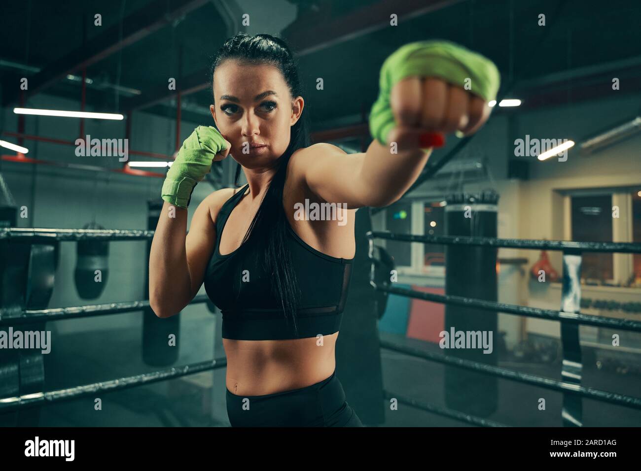 Athletic woman during fighting training on boxing ring wearing green bandages on hands Stock Photo