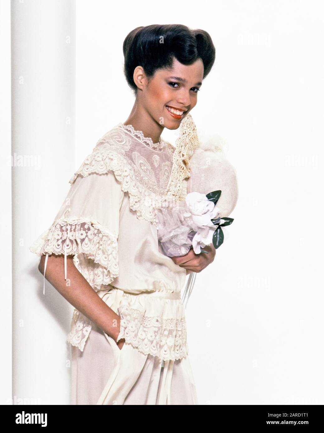 1980s 1970s SMILING AFRICAN-AMERICAN WOMAN  WEARING LACE & RUFFLE BLOUSE SKIRT HOLDING HAT WHITE CAMELLIAS LOOKING AT CAMERA - ks17840 PHT001 HARS CELEBRATION EVENT HEALTHINESS COPY SPACE HALF-LENGTH VEIL CONFIDENCE CEREMONY BRIDAL EYE CONTACT GOALS DREAMS HAPPINESS CHEERFUL BRIDES STYLES CUSTOM AFRICAN-AMERICANS AFRICAN-AMERICAN AND EXCITEMENT TRADITION OCCASION BLACK ETHNICITY PRIDE BLOUSE OCCUPATIONS POSING SMILES CONNECTION CONCEPTUAL JOYFUL RUFFLE STYLISH MAID OF HONOR MODELLING FASHIONS MODELING POSE YOUNG ADULT WOMAN OLD FASHIONED AFRICAN AMERICANS Stock Photo