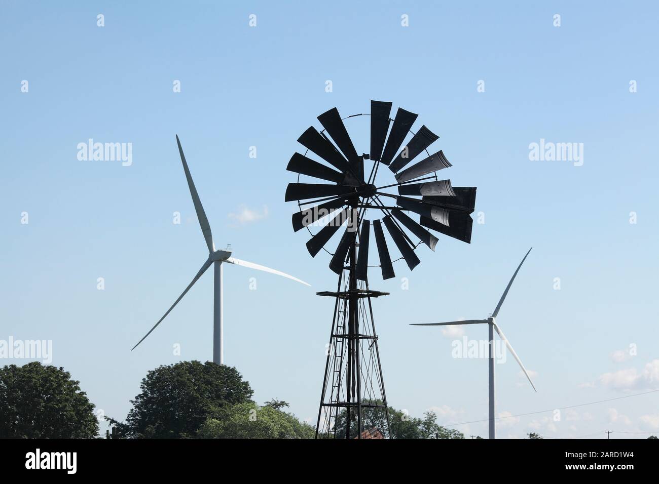 Old and new technology for harnessing the power of the wind: an old, disused multi-vaned wind pump for raising water flanked by modern wind turbines. Stock Photo