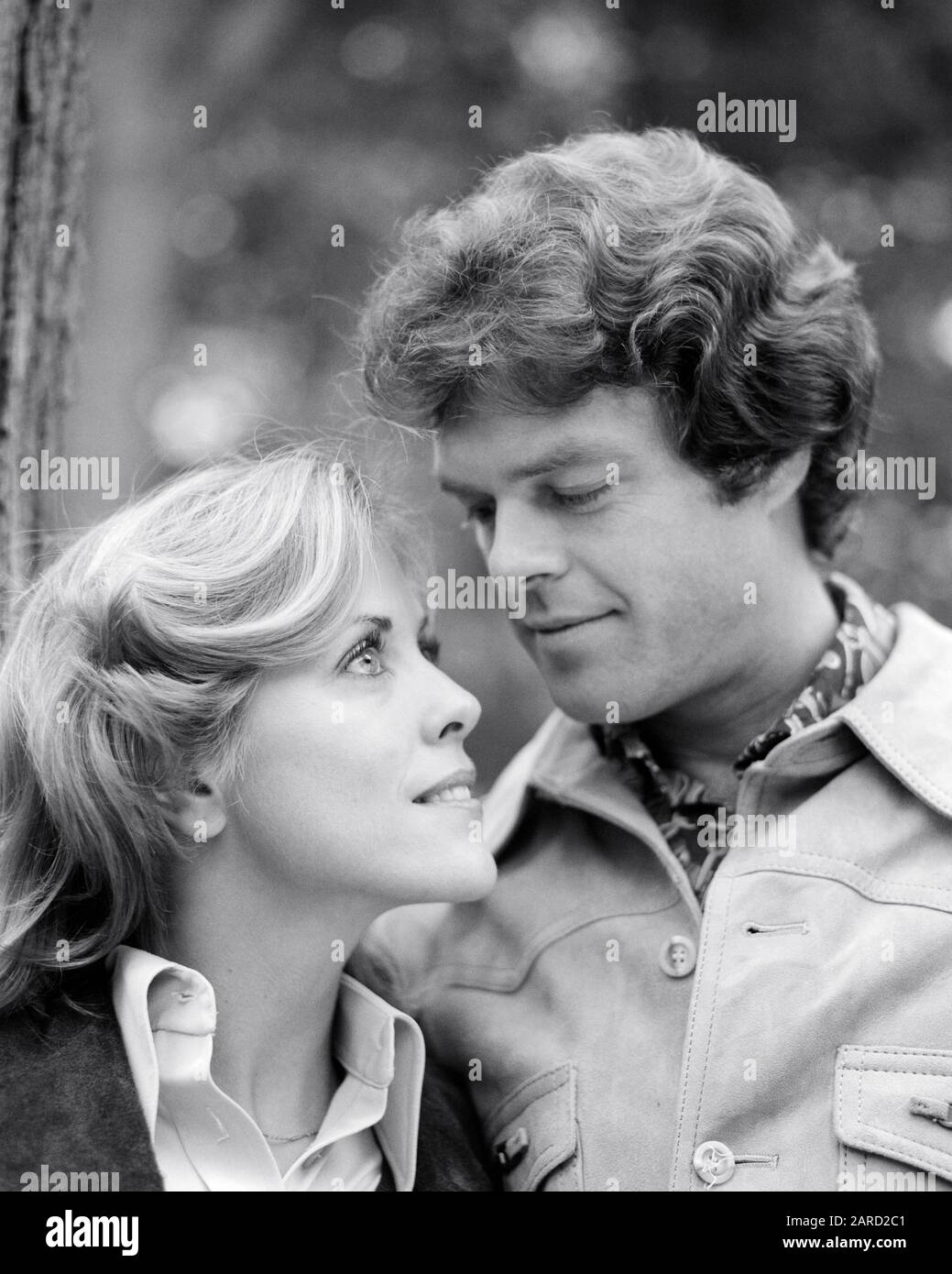 1970s HANDSOME YOUNG MAN LOOKING ADMIRINGLY INTO THE FACE OF STARRY EYED YOUNG BLOND WOMAN AUTUMN OUTDOORS pic