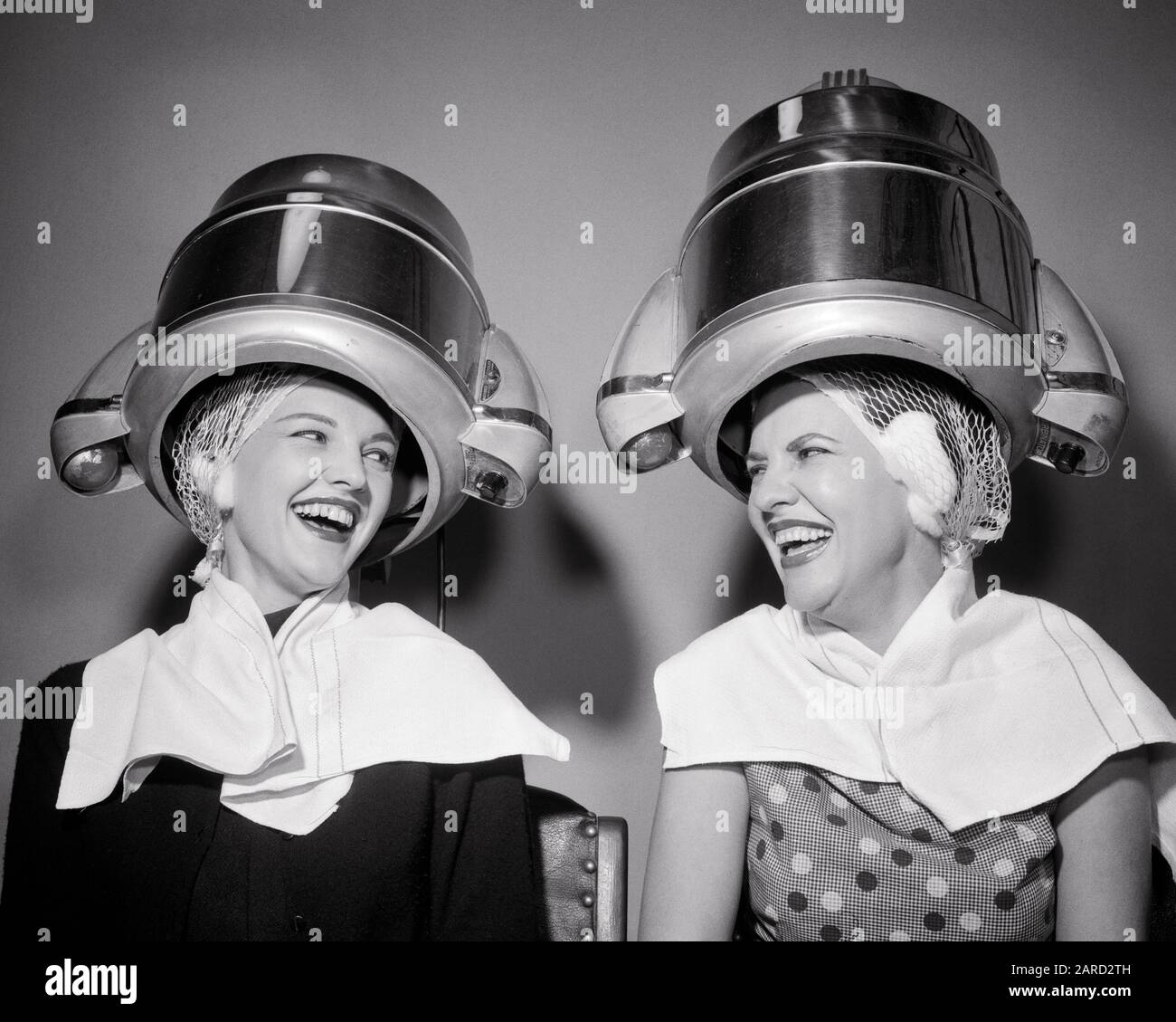 1950s TWO LAUGHING WOMEN SITTING UNDER BEAUTY SALON HAIR DRYERS WEARING  HAIR NETS TOWELS TALKING GOSSIP TOGETHER - s8921 DEB001 HARS FACIAL STYLE  COMMUNICATION LAUGH YOUNG ADULT COMIC SALON INFORMATION PLEASED JOY