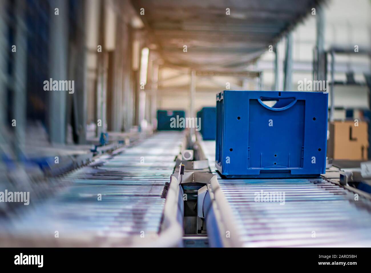 Blue boxes in a large, fully automated logistics warehouse run on a conveyor belt. Background is