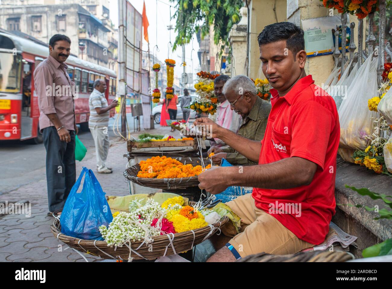 Mumbai, India - December 17, 2017: Vendors preparing marigold necklaces in front of a passerby in a busy street Stock Photo